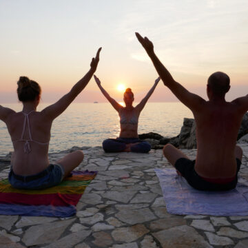Drei Personen beim Yoga am Meer mit Sonnenuntergang
